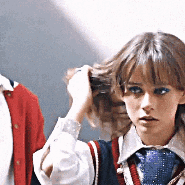 a girl adjusts her hair while wearing a tie