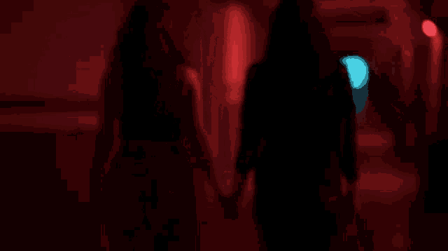 two women are holding hands in a dark hallway with red lights