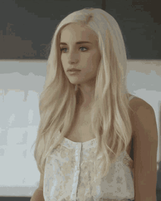 a woman with long blonde hair and blue eyes is wearing a white tank top