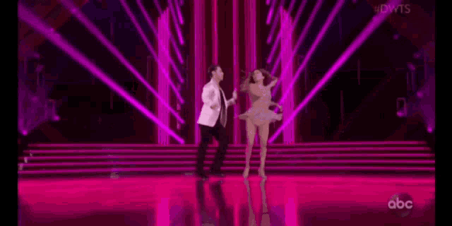 a man and a woman are dancing on a stage with a purple background .