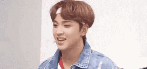 a young man wearing a denim jacket and a headband is smiling and looking at the camera .