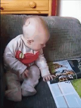 a baby is sitting on a couch looking at a magazine with the word e on it
