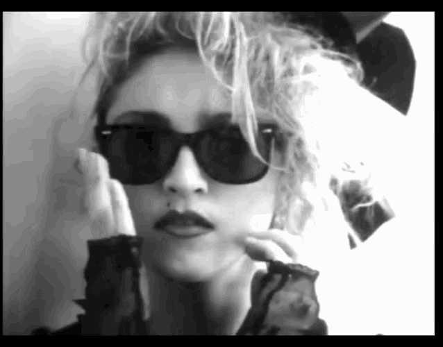a woman wearing sunglasses and a mustache looks at the camera in a black and white photo