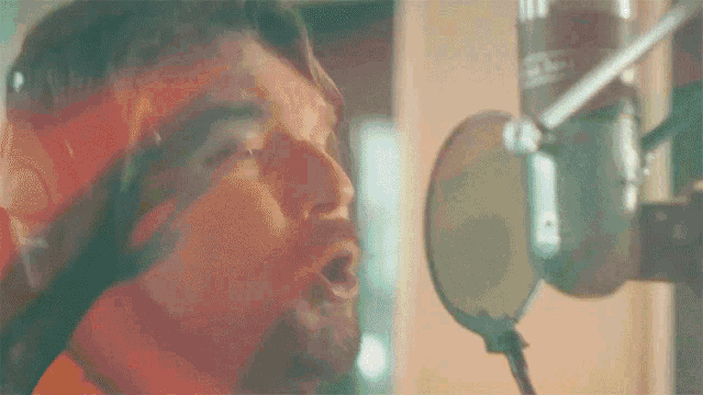 a close up of a man singing into a microphone in a recording studio