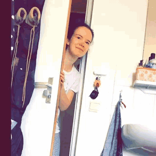 a woman is peeking out from behind a door