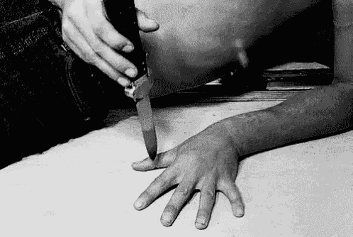 a black and white photo of a person holding a knife over another person 's hand .