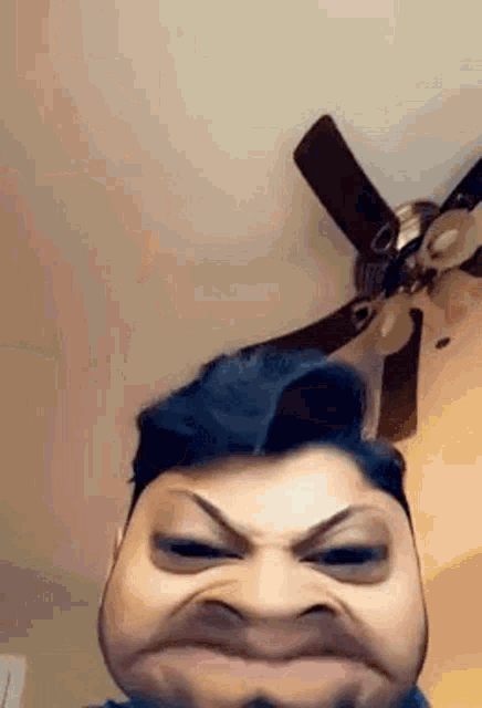 a man is making a funny face while standing in front of a ceiling fan .