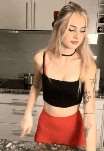 a woman in a black crop top and red skirt stands in a kitchen