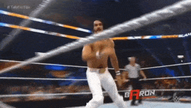 a man without a shirt is standing in a wrestling ring with a referee .