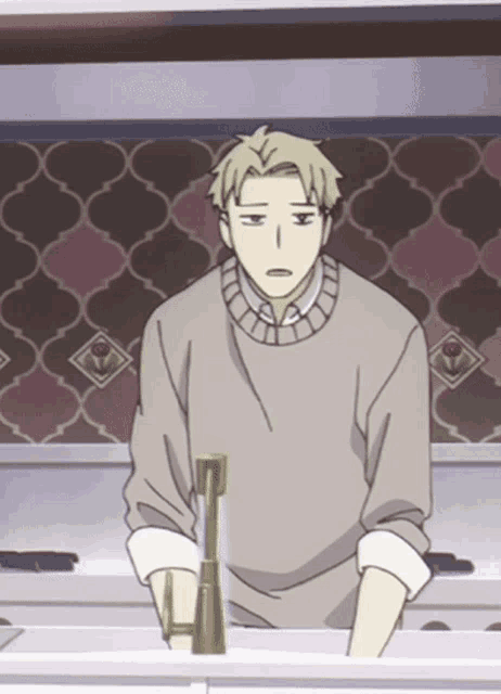 a man in a grey sweater is standing in front of a kitchen counter