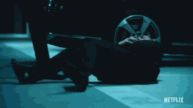 a person laying on the ground in front of a car with netflix written on the bottom right