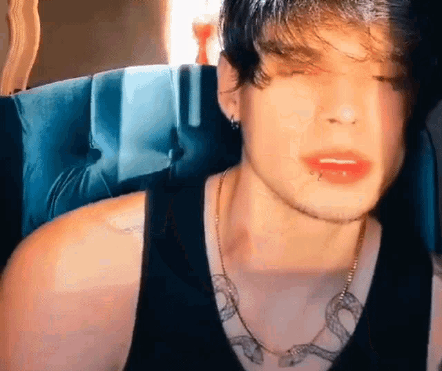 a young man with a snake tattoo on his chest is wearing a black tank top and a snake necklace .