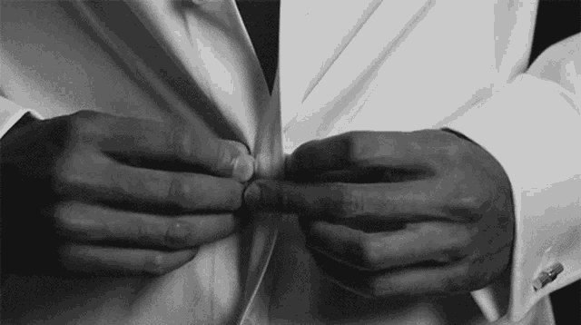 a man in a white shirt and black tie is adjusting his shirt buttons .