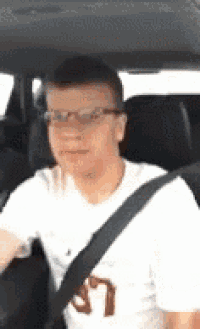 a man is sitting in the driver 's seat of a car wearing glasses and a seat belt .