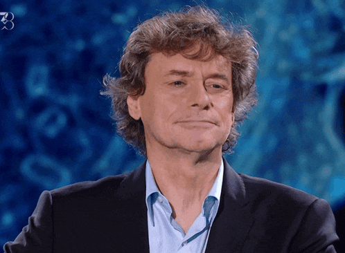 a man with curly hair wearing a suit and blue shirt