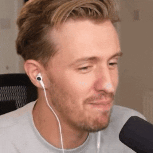 a man with a beard is wearing earbuds and talking into a microphone .