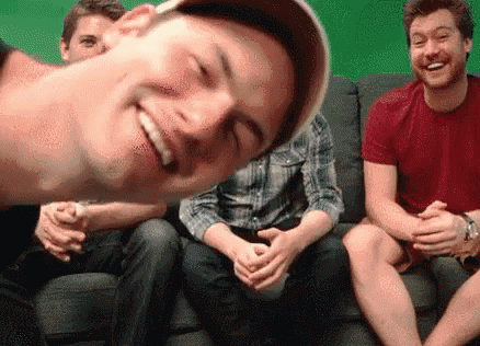 a group of men are sitting on a couch and one of them is smiling at the camera .