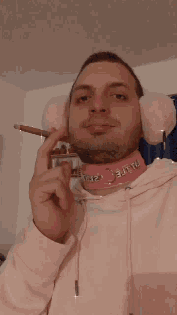 a man wearing pink ear muffs and a pink choker smoking a cigarette