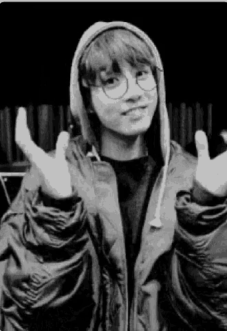 a black and white photo of a young man wearing a hoodie and glasses .