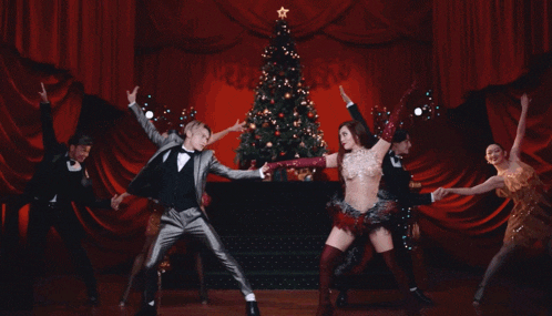 a man in a tuxedo is dancing with a woman in a red dress in front of a christmas tree .