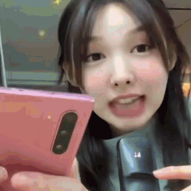a woman is holding a pink cell phone in her hand and smiling at the camera .