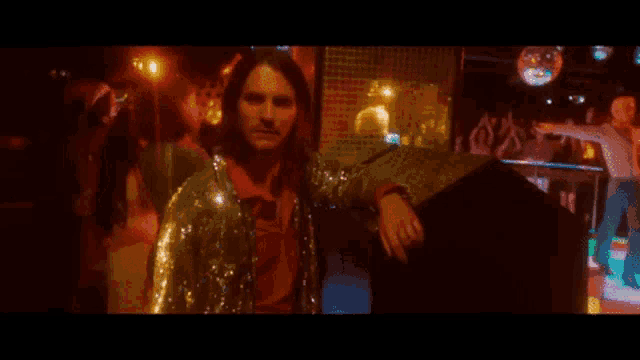 a man in a sequined jacket is standing in a disco club