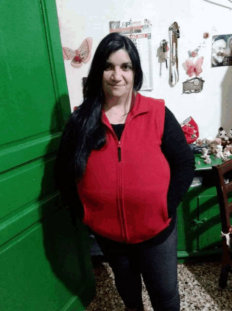 a woman wearing a red vest stands in front of a wall with a calendar on it
