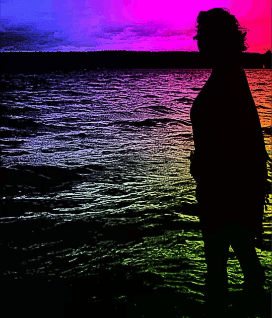 a silhouette of a woman standing in front of a rainbow colored water