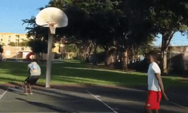two men are playing basketball in a park and one of them is wearing red shorts