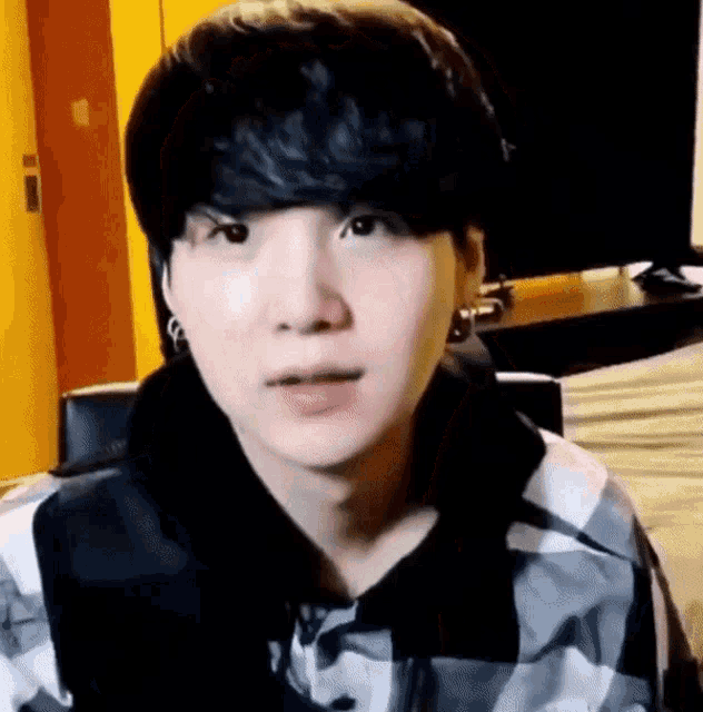 a close up of a person 's face wearing a plaid shirt and earrings .