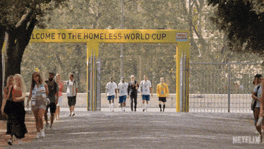 a group of people walking under a welcome to the homeless world cup sign