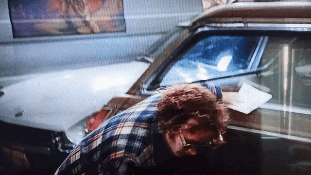 a man in a plaid shirt is standing next to a car with a license plate that says ' aa ' on it