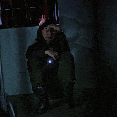 a woman is sitting in a dark room with her hand on her head