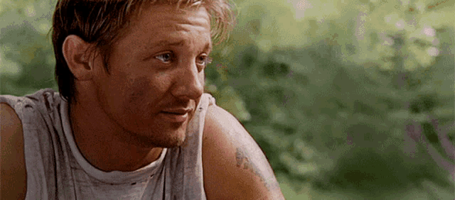 a man with a tattoo on his arm is wearing a white tank top