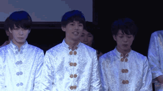 a group of young men are standing in a line wearing white jackets with gold buttons