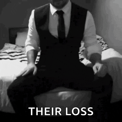 a man in a suit and tie is sitting on a bed with the words their loss written below him
