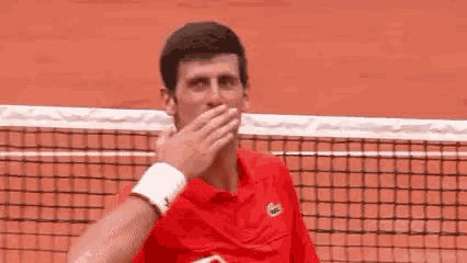 a man in a red shirt is standing on a tennis court giving a thumbs up .