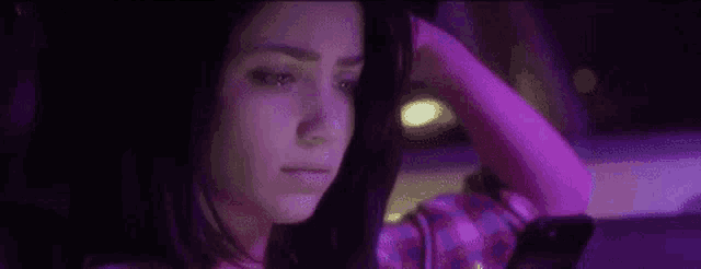 a woman is crying while looking at her phone in a dark room with purple lights .
