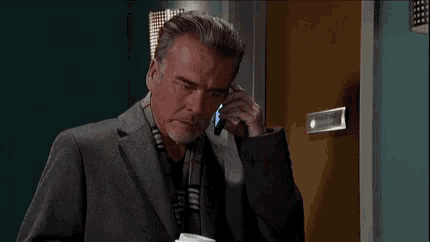 a man in a suit and scarf is talking on a cell phone in front of a door .