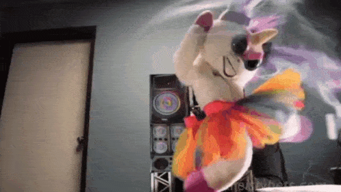 a stuffed animal in a unicorn costume is dancing in front of speakers .