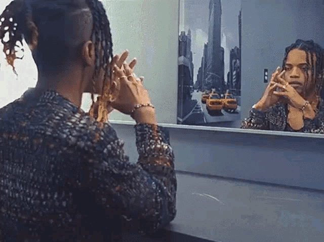 a woman is looking at her reflection in a mirror with a picture of new york taxis on the wall behind her