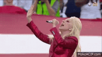 a woman in a red jacket is singing into a microphone in front of a crowd .