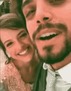 a man and a woman are smiling for a picture . the man has a beard and the woman is wearing a dress .