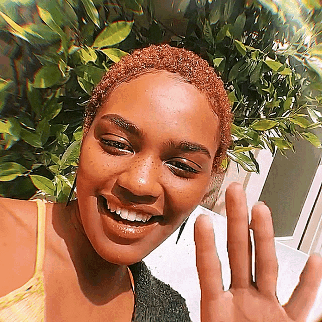a woman with red hair and freckles is smiling and waving at the camera