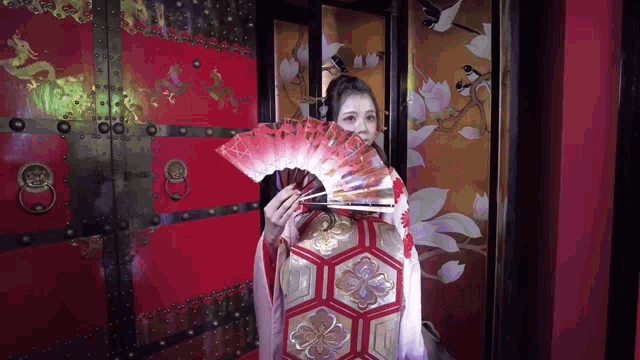 a woman in a kimono is holding a fan in front of a door
