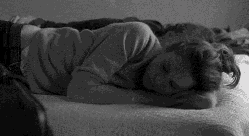 a black and white photo of a woman sleeping on a bed .
