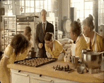 a group of people are standing around a tray of cookies in a kitchen .