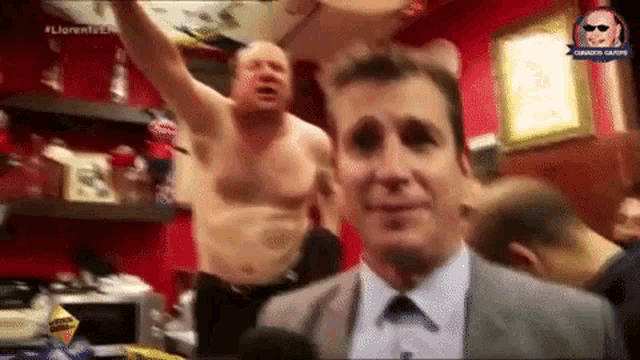 a shirtless man in a suit is being interviewed by a man in a suit