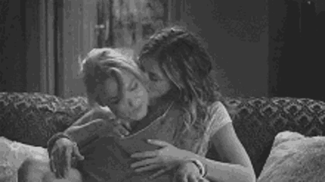 a black and white photo of a couple hugging on a couch .