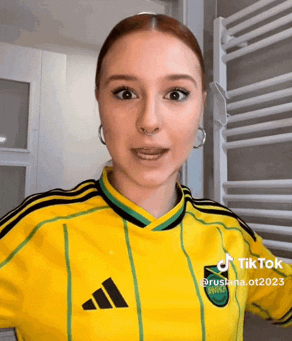 a woman wearing a yellow and green adidas jersey looks surprised